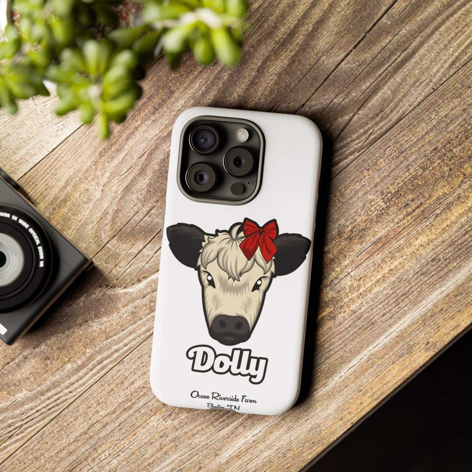 Farmhouse Chic Phone Case with Dolly Red Bow Cow design on wooden table.