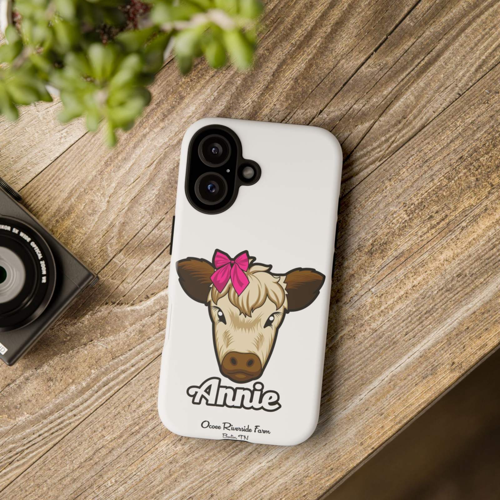 Cute cow phone case with red bow on wooden table, perfect farm animal lover gift.