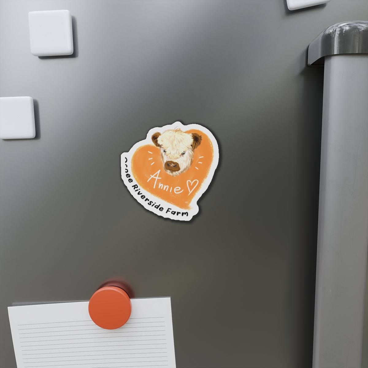 Cute Cow Design Die-Cut Magnet with a cow illustration on an orange heart background, displayed on a gray refrigerator door.