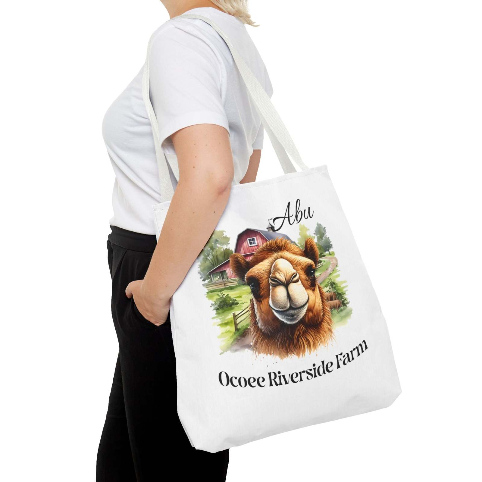 White eco-friendly Abu Camel Tote Bag featuring farm-themed artwork, worn by person with white t-shirt and black pants.