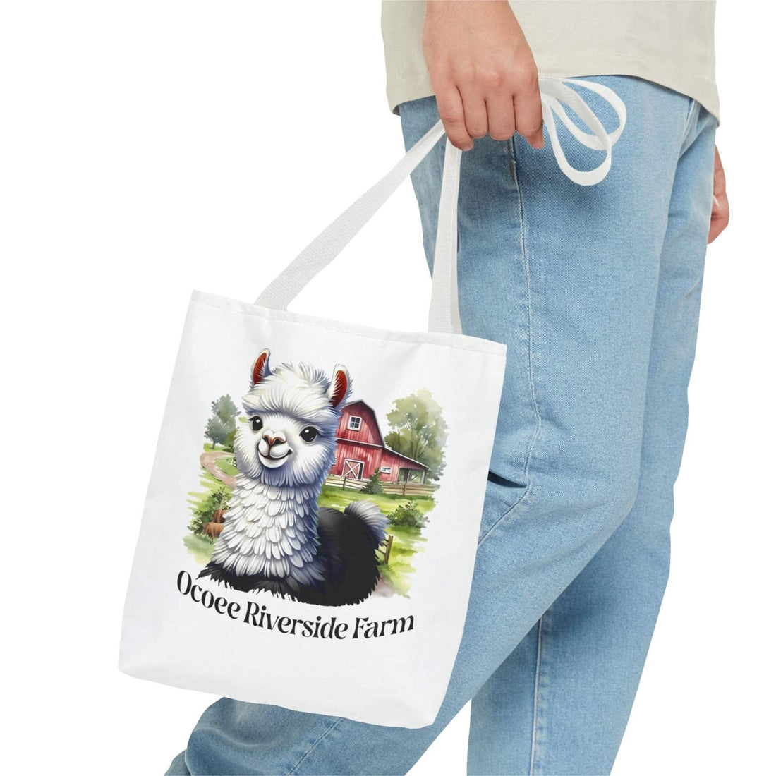 White eco-friendly Alpaca Tote Bag with Ocoee Riverside Farm design, held by person wearing blue jeans.