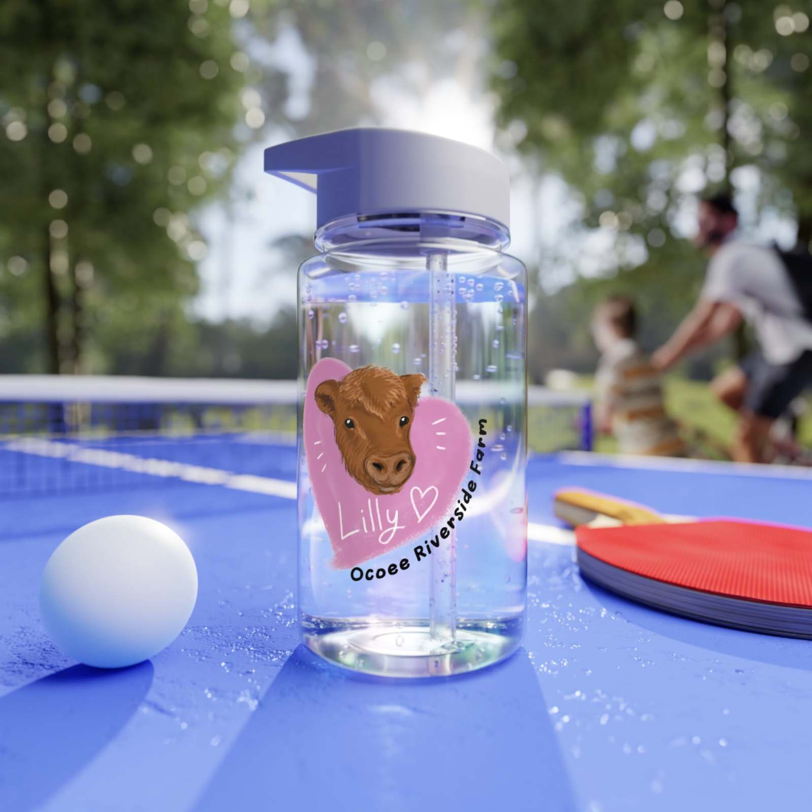 Clear Cow Farm Water Bottle with straw, personalized with cow design and name, on blue outdoor table with ping pong items