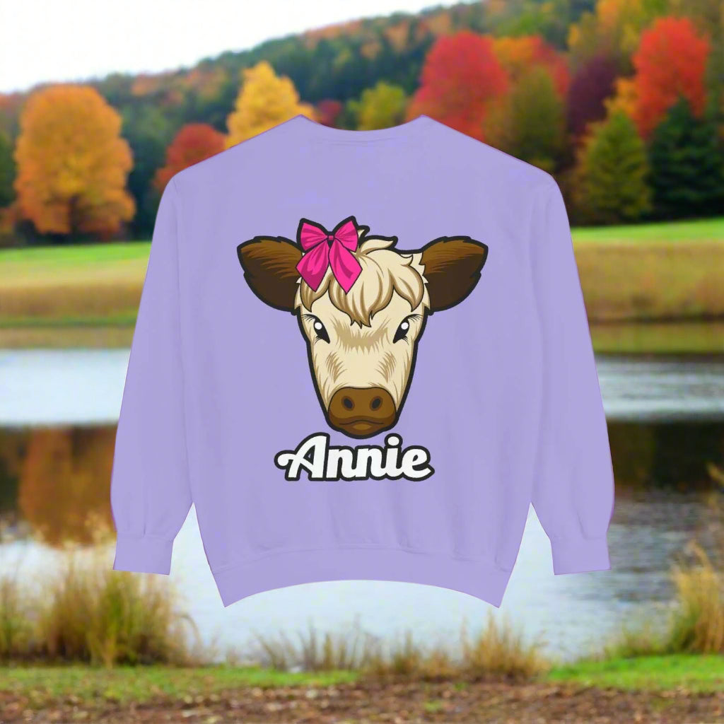 Cute farm animal sweatshirt featuring Annie the cow with a red bow on a purple background.