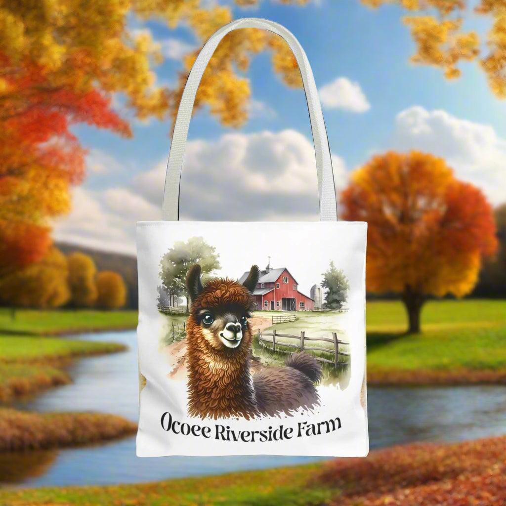 White tote bag featuring a cute llama illustration with a rustic farm background and the text "Ocoee Riverside Farm"