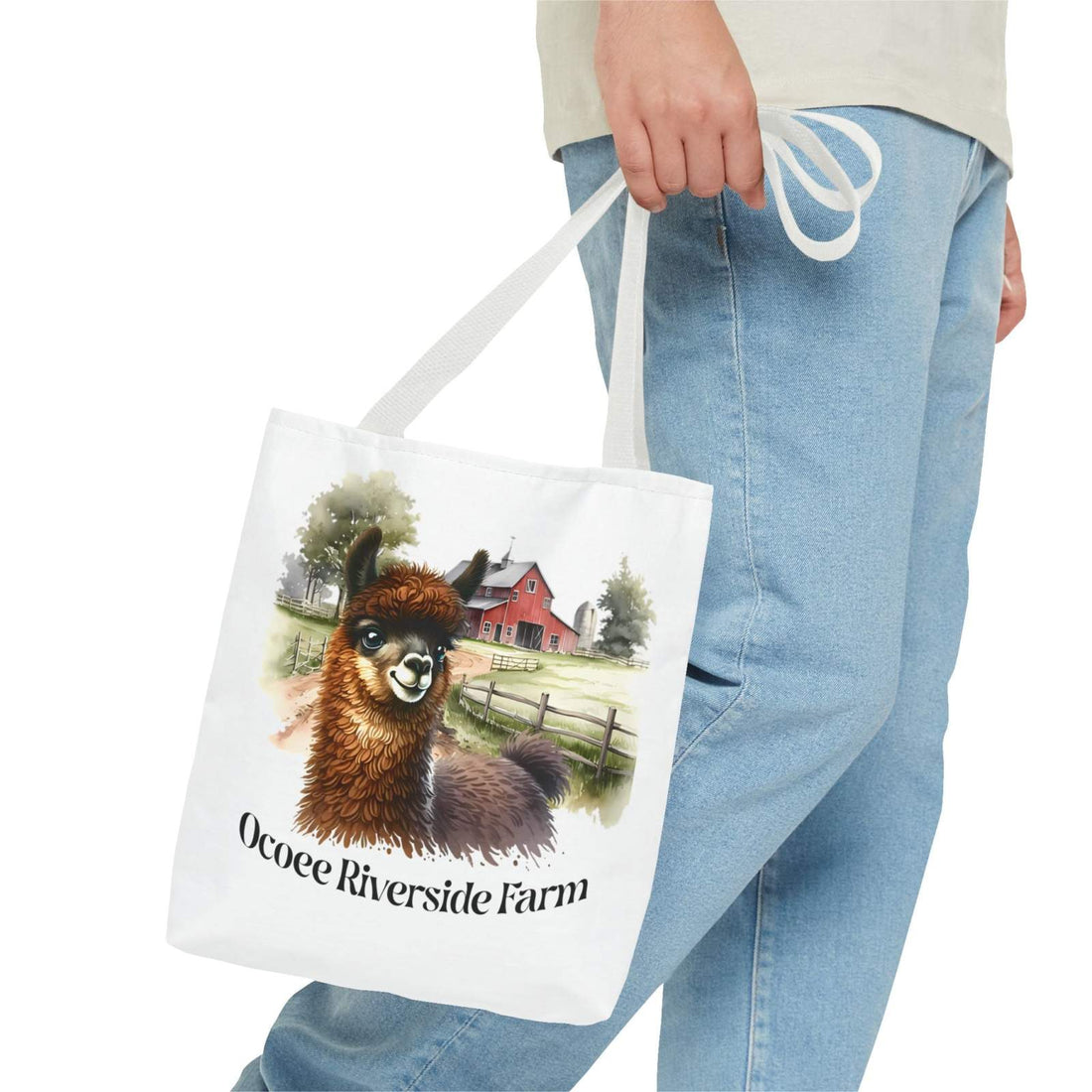 Person holding a white tote bag featuring a cute llama illustration and a red barn with text "Ocoee Riverside Farm"