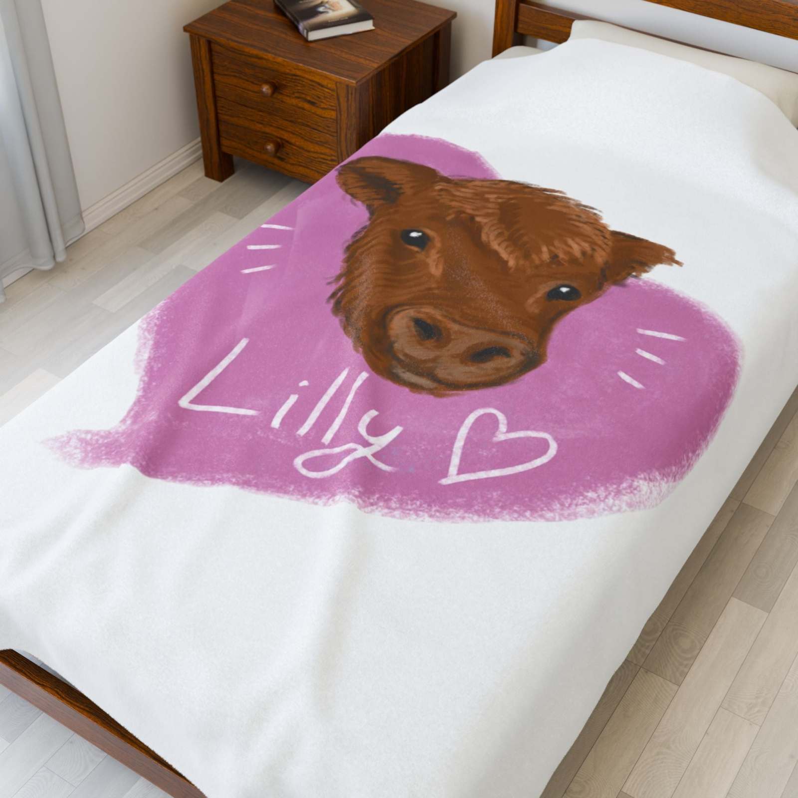 White plush blanket with a cute brown cow face and pink heart design reading "Lilly" on a bed