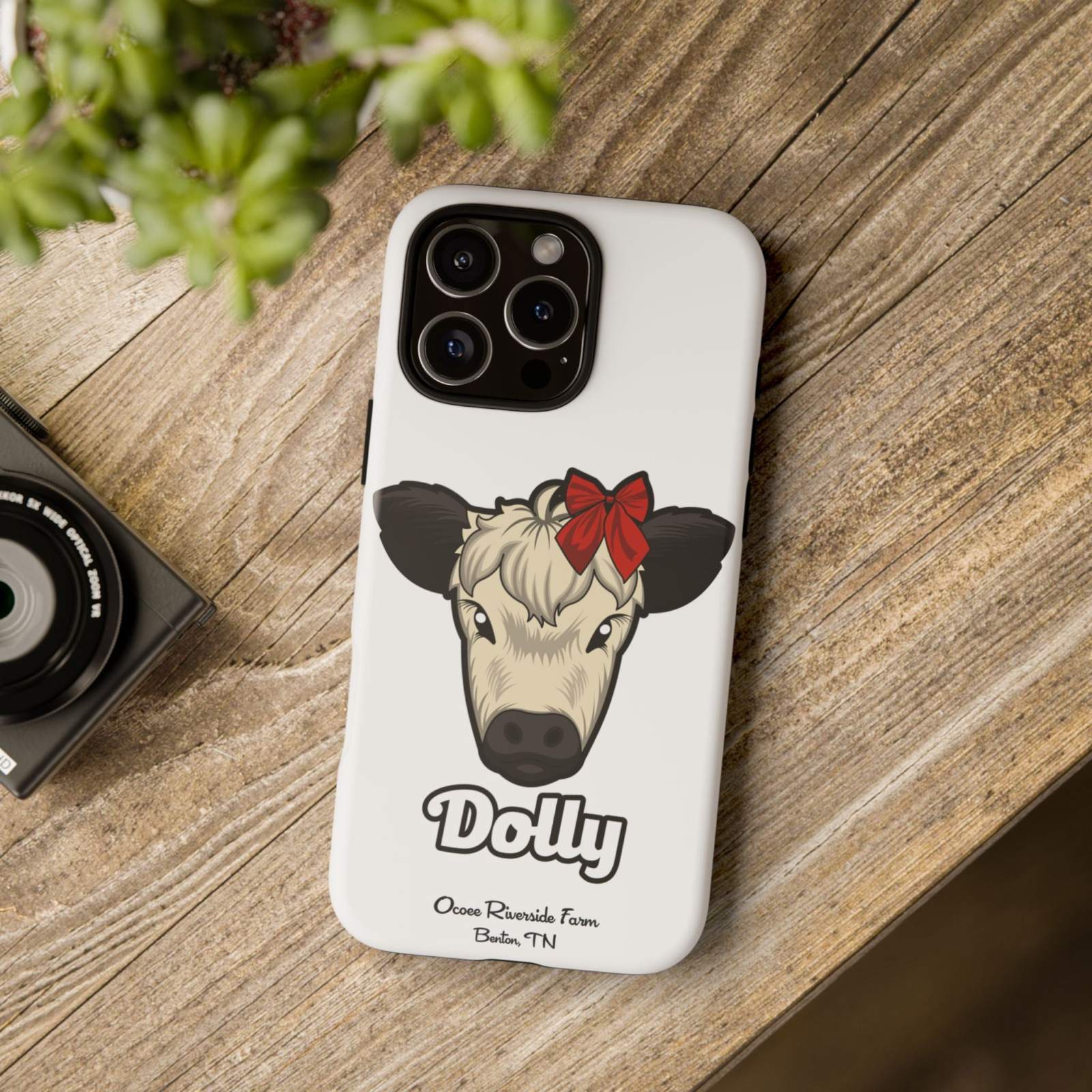 Farmhouse Chic Phone Case with cow illustration and red bow, on wooden surface.