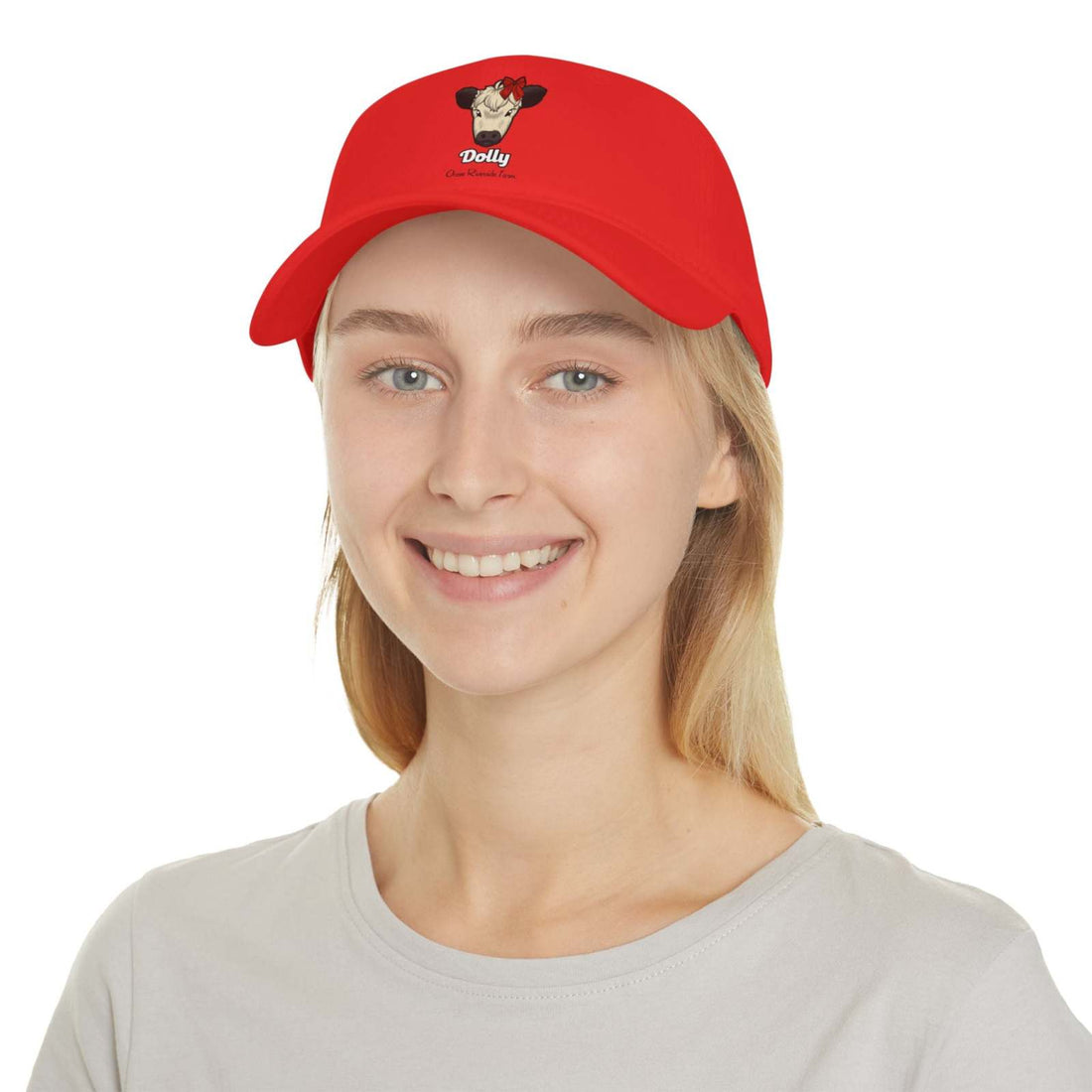 Red low profile cow baseball cap with embroidered cow named Dolly wearing a red bow, worn by smiling woman