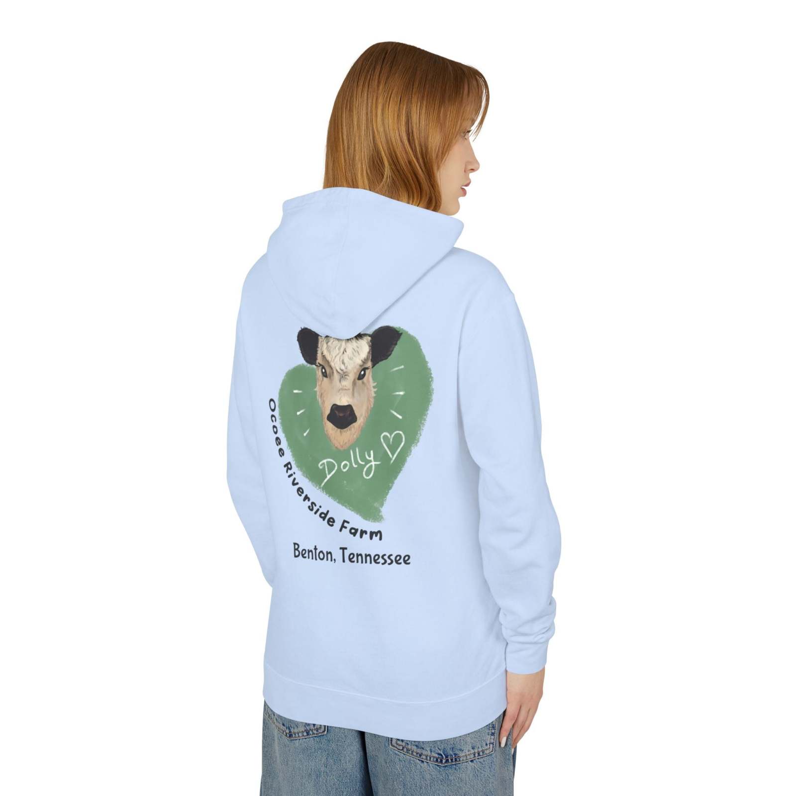 Light blue Cozy Cow Hoodie featuring a cow graphic and "Ocoee Riverside Farm" text on the back, worn by a woman.