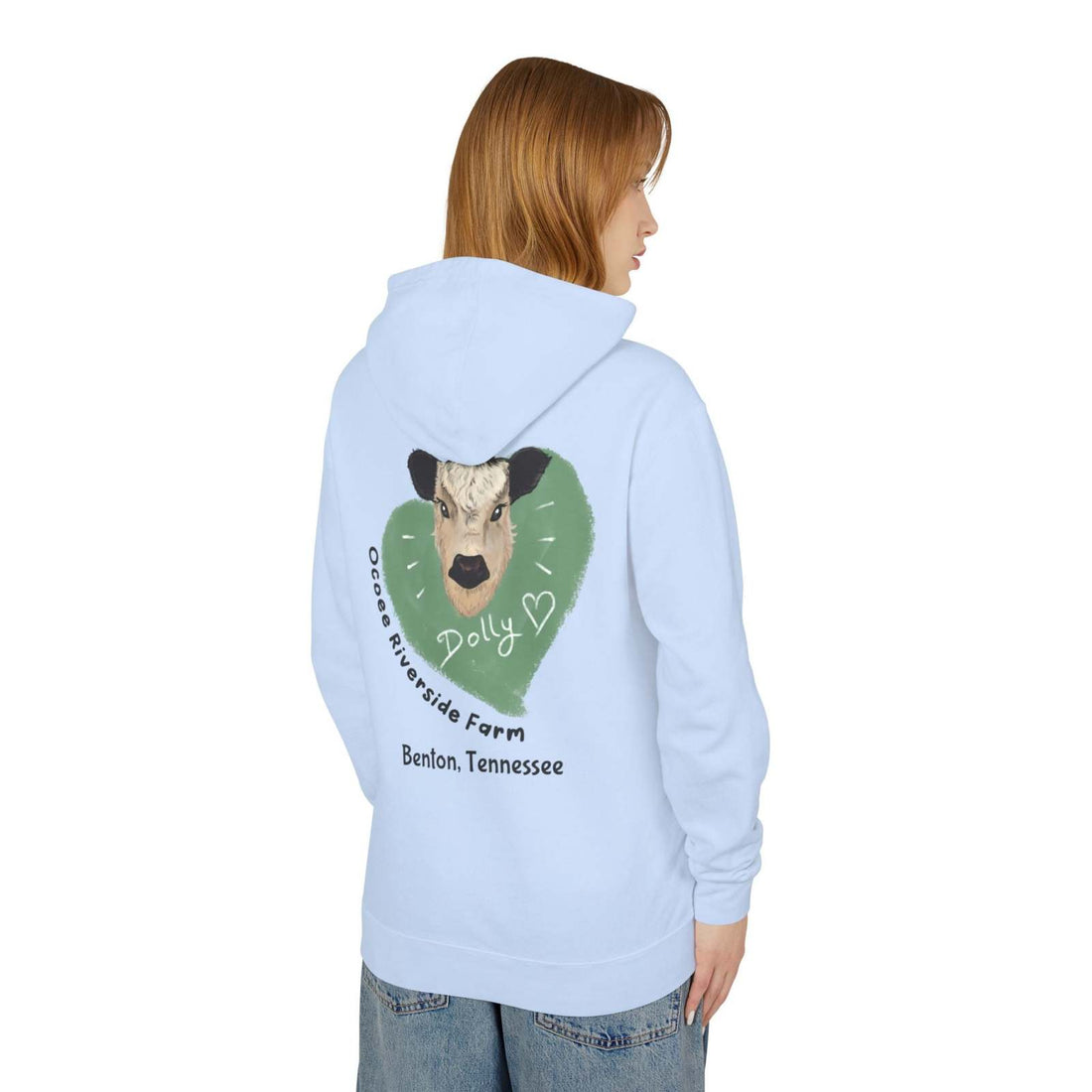 Light blue Cozy Cow Hoodie featuring a cow graphic and "Ocoee Riverside Farm" text on the back, worn by a woman.