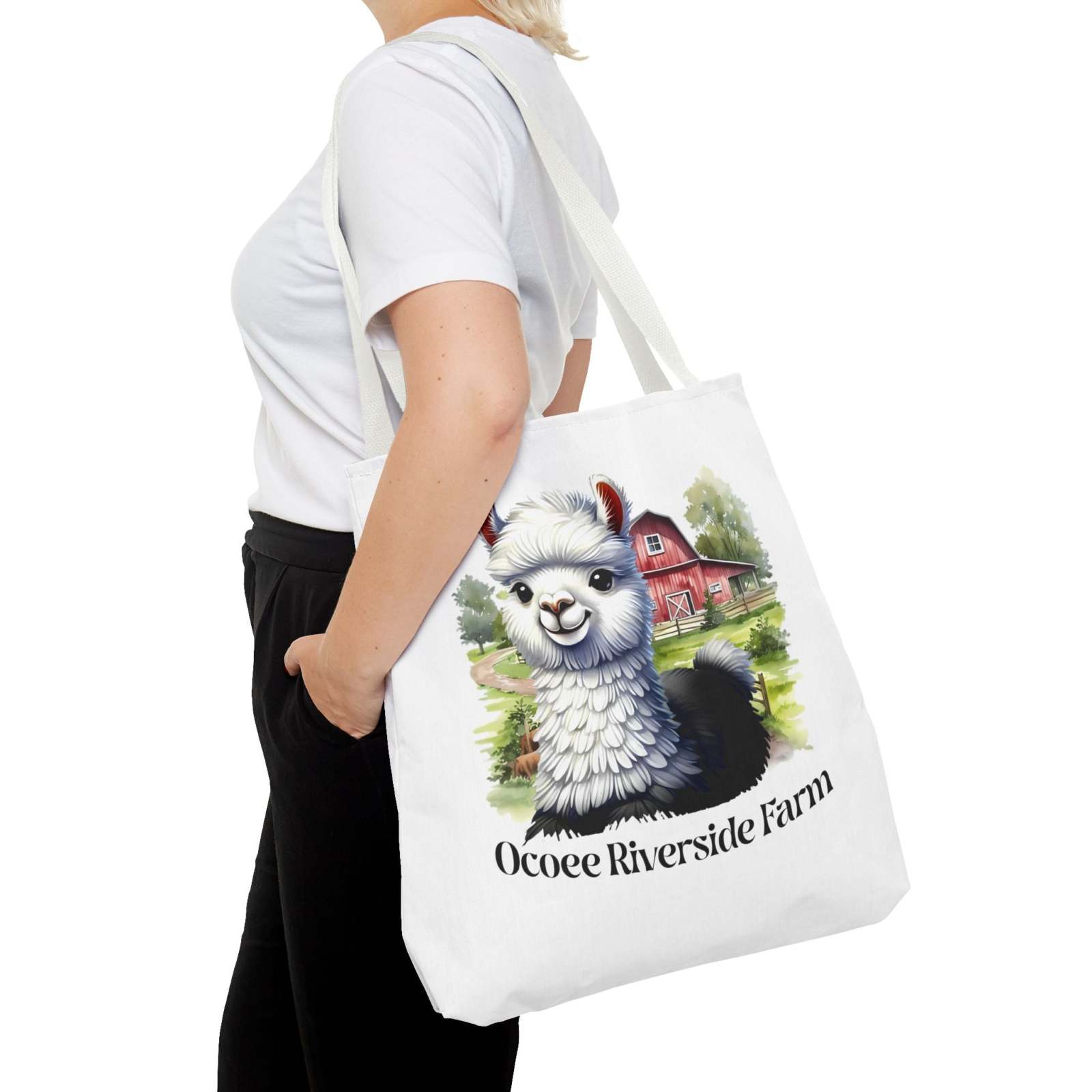 White eco-friendly Alpaca Tote Bag from Ocoee Riverside Farm featuring a colorful alpaca and farm illustration, carried by a woman