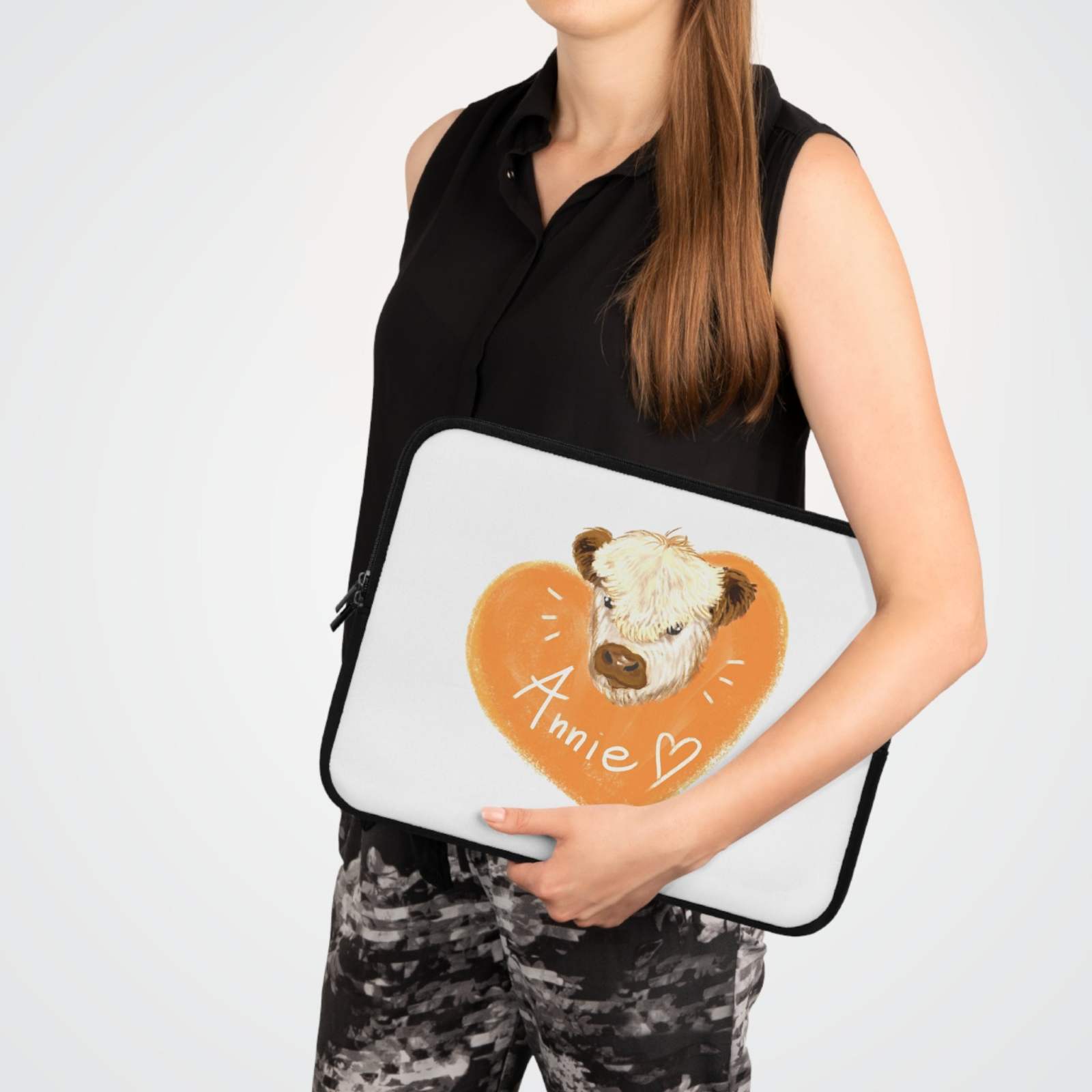 Woman holding custom cow laptop sleeve with heart design and name Annie on white background